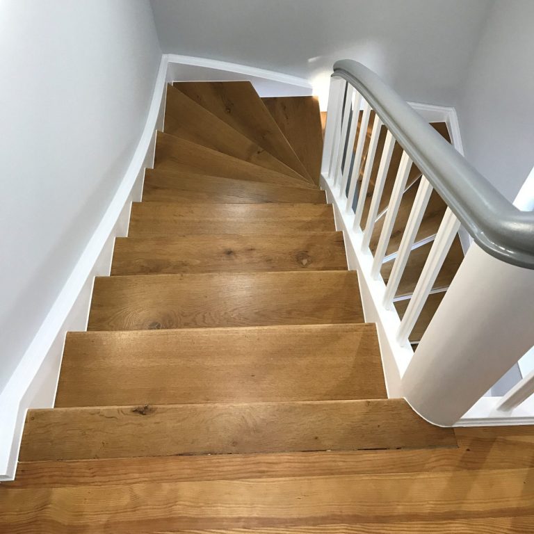 Holztreppe mit geländerte, die nach unten führt, auf hellen Wänden.