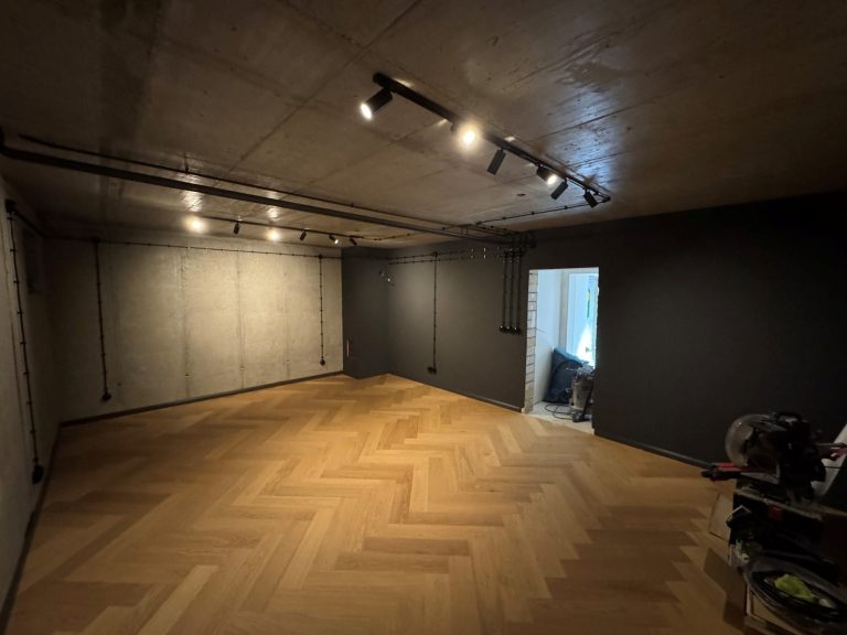 Leerer Raum mit Holzfußboden, Betonwänden und Spotlights an der Decke.